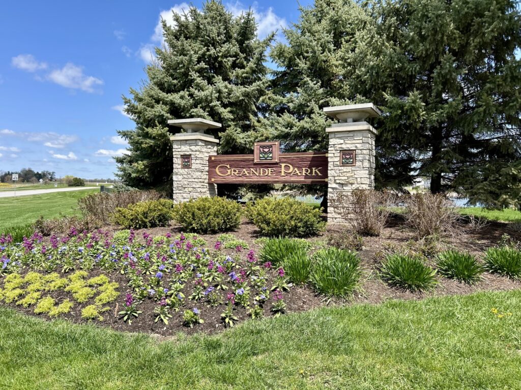 an entrance signage of Grande Park surrounded by trees and flowers