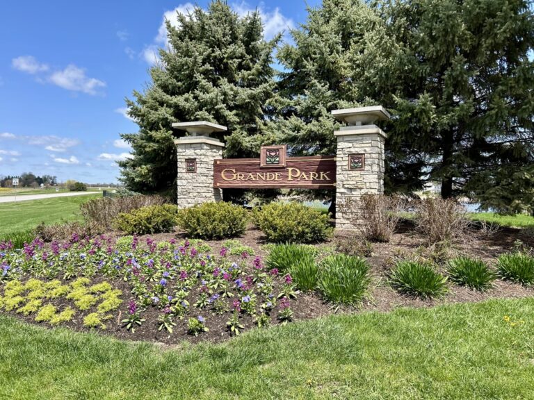an entrance signage of Grande Park surrounded by trees and flowers