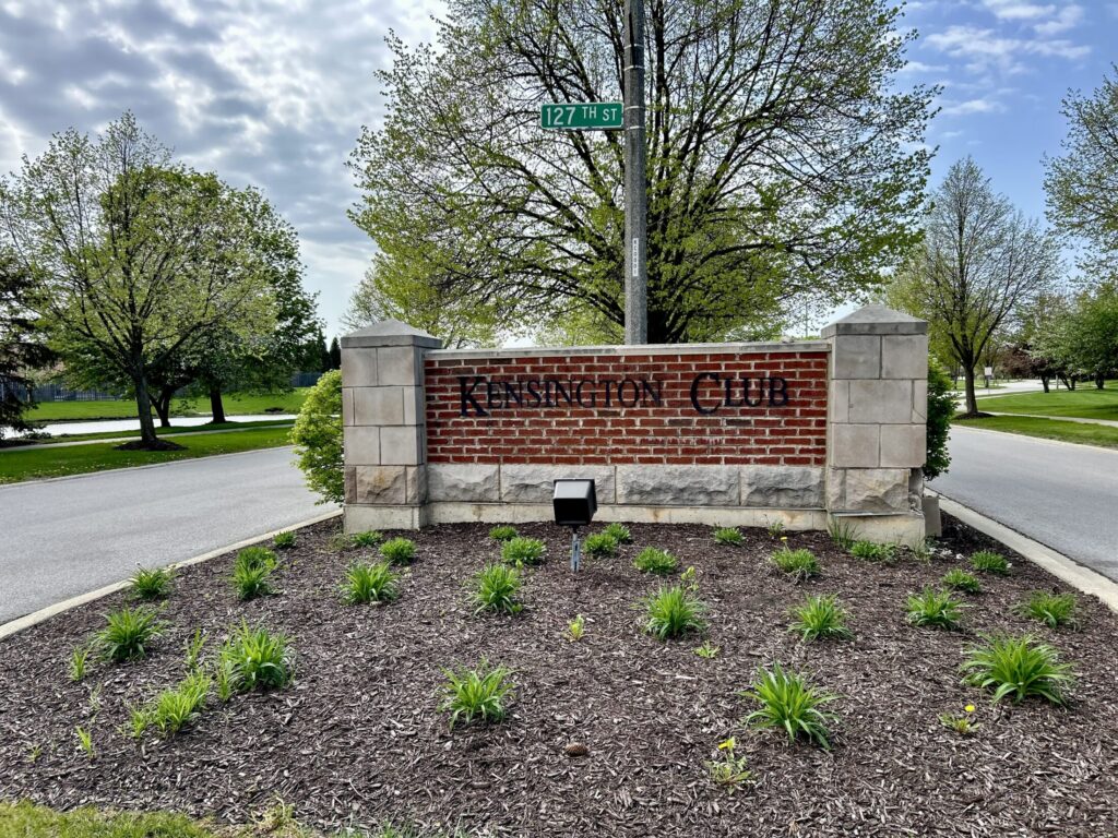 a sign of Kensington Club on a small brick wall with a tree on the back